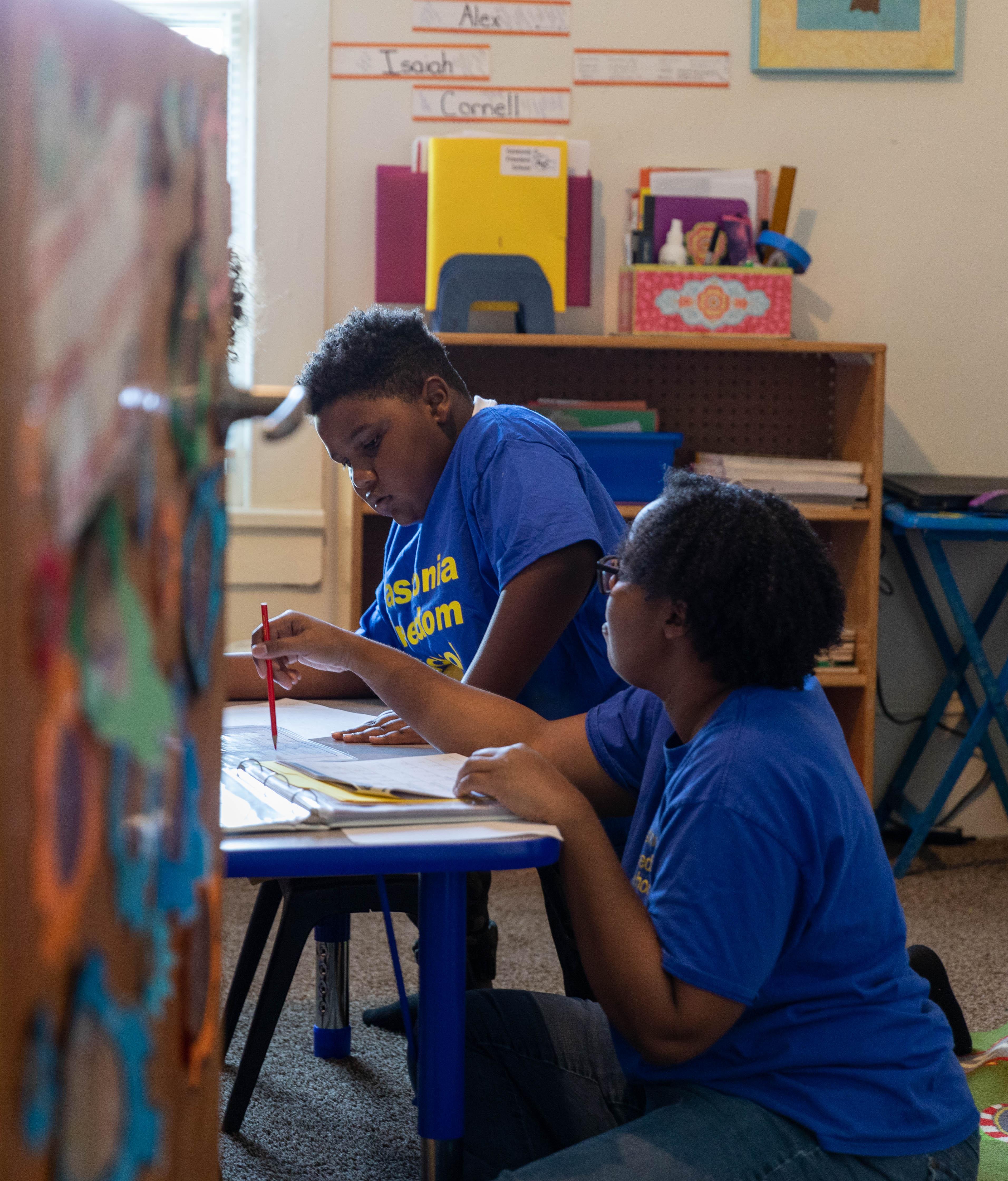 a student and adult sitting on the floor at a short table looking at papers