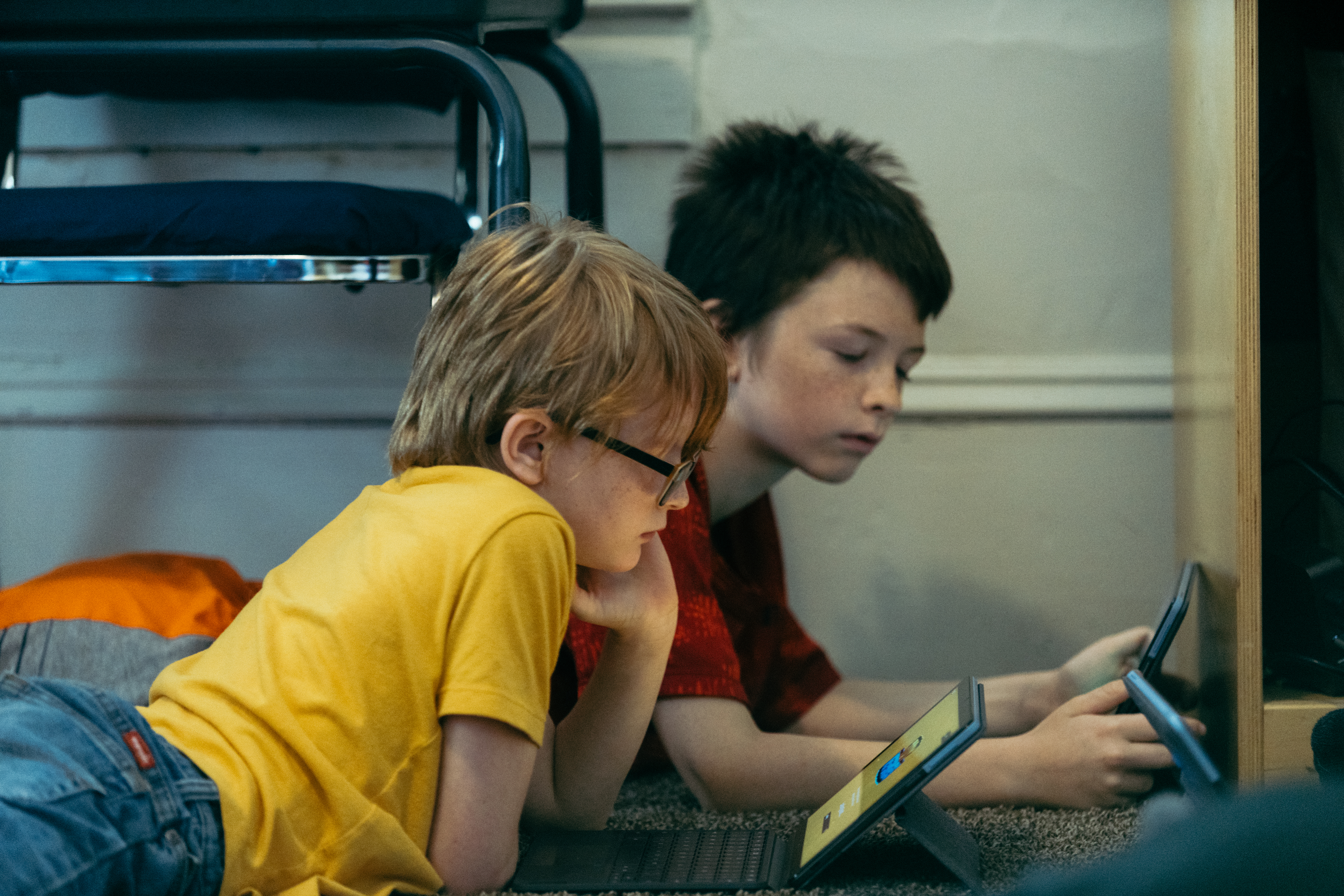 dos niños tendidos en el suelo mirando tabletas
